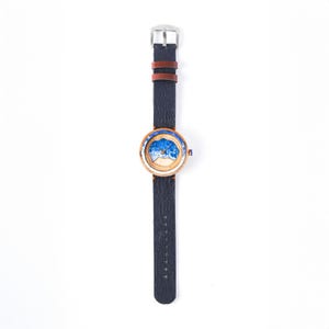 May include: A wooden wristwatch with a blue and white ocean wave design on the face. The watch has a black leather band with a brown leather accent.