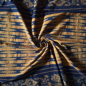 May include: A blue and gold fabric with a woven pattern. The fabric is folded and draped, creating a swirling effect.
