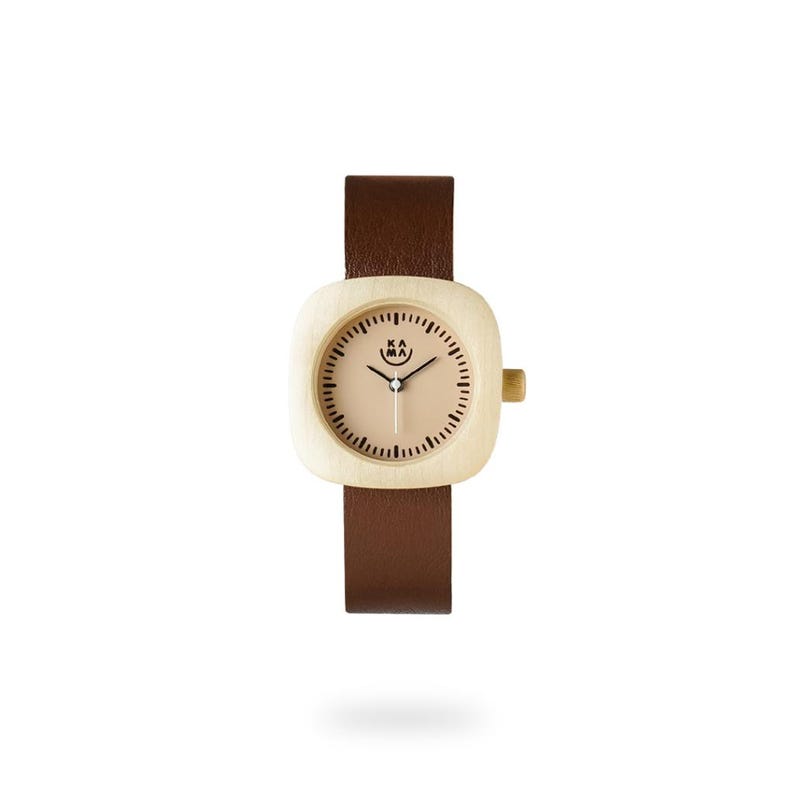 May include: A wristwatch with a light wood-colored square face and a brown leather band. The watch face has a light tan background with black minute markers and hands. The watch has the text "KA MA" on the face.