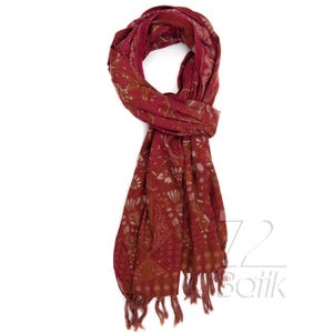 May include: A burgundy scarf with a floral pattern and fringe. The scarf is made of a lightweight fabric and features a repeating design of white flowers and leaves. The scarf is draped and folded, showcasing its length and texture.