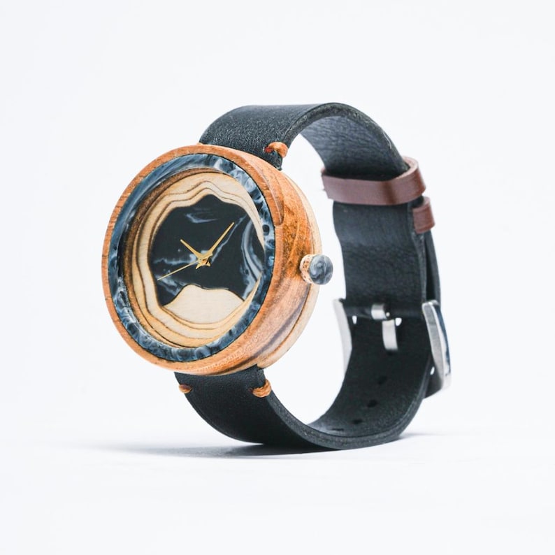 May include: A wooden wristwatch with a black and white marbled face and a black leather band.
