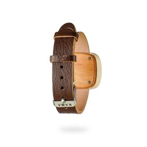May include: A wristwatch with a brown leather band and a light-colored wooden watch face. The watch face is square with rounded corners and is attached to the band with silver screws. The buckle is silver and has the word "KAMA" engraved on it.