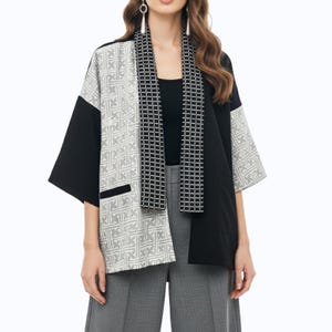 May include: A black and white patterned kimono-style jacket with three-quarter sleeves. The jacket features a geometric design on the front panels and sleeves, with a contrasting black fabric on the back and sleeves. A matching scarf is draped over the front.