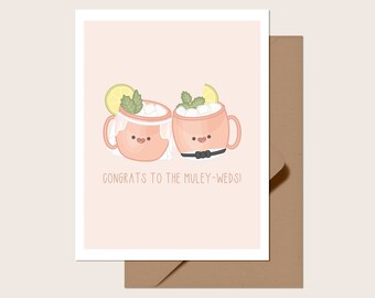 May include: A pink wedding card with two illustrated mugs with faces and a lime wedge. The text reads "Congrats to the Muley-Weds!"