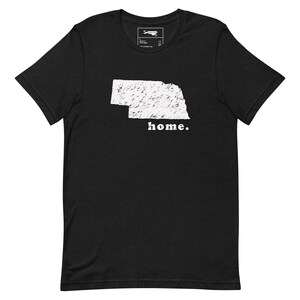 Puede incluir: Camiseta negra con un contorno blanco del estado de Nebraska y la palabra "home." impresa debajo.