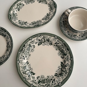 May include: A set of four green and white floral patterned ceramic plates, including a large oval platter, a round dinner plate, a smaller round plate, and a saucer with a matching teacup.