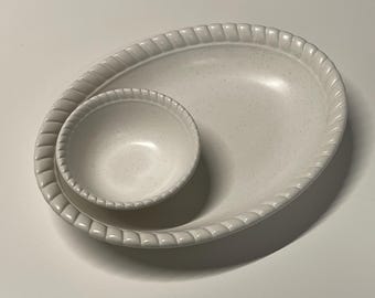 May include: A white oval serving dish with a raised rim and a smaller white bowl inside. Both pieces have a speckled texture.