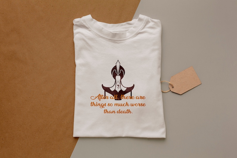 May include: White t-shirt with a brown graphic of a character from the movie Aladdin. The graphic is of the character Jafar, sitting on his throne. The text below the graphic reads "After all, there are things so much worse than death."