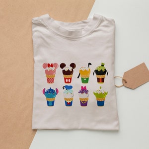 Puede incluir: Camiseta blanca con un gr&aacute;fico colorido de varios personajes de Disney en forma de conos de helado. Los personajes incluyen Mickey Mouse, Minnie Mouse, Stitch y otros.