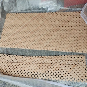 a clear plastic bag containing two wooden boards with a lattice pattern. The boards are arranged in a way that they appear to be folded or stacked on top of each other.