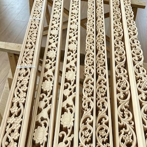 Può includere: Diversi pannelli di legno chiaro con intagli floreali e fogliari dettagliati. I pannelli, possibilmente non rifiniti, sono disposti uno accanto all'altro, mostrando l'intricata maestria artigianale. Le incisioni presentano una varietà di motivi floreali e fogliari.