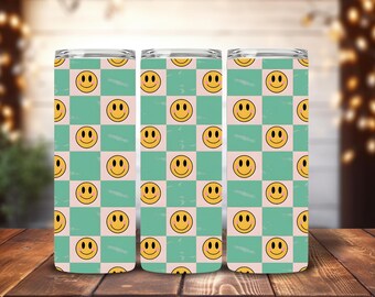 May include: Three stainless steel tumblers with a repeating pattern of yellow smiley faces on a checkerboard background of light pink and teal. The tumblers are cylindrical and have a clear lid.