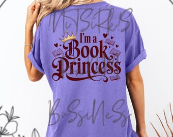 Puede incluir: Camiseta de color lila con la frase "I'm a Book Princess" en borgoña. El diseño incluye una corona dorada, corazones e ilustraciones de libros. La camiseta tiene mangas cortas.
