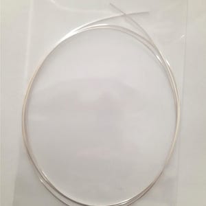 May include: A collection of thin, silver-coloured wire, coiled within a clear plastic package. The wire has a smooth, reflective surface, indicating a metallic material. The transparent packaging allows for clear visibility of the contents.