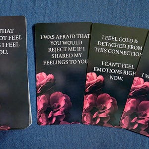 May include: A deck of oracle cards with a dark background and pink floral accents. Each card features a different phrase in white text. The phrases include: "I know that you may not feel for me as I feel for you."