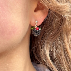 Puede incluir: Un par de pendientes de plata con un dije de mora negra y roja.