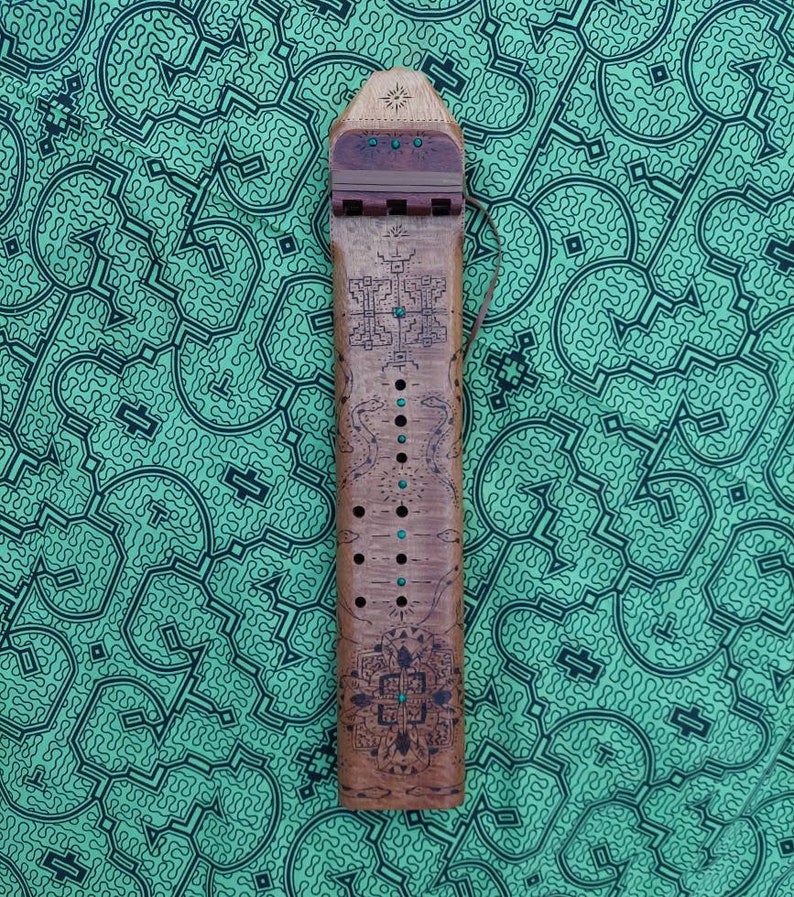May include: A wooden musical instrument with a carved design and turquoise accents. The instrument has a series of holes along the side and a string attached to the top.