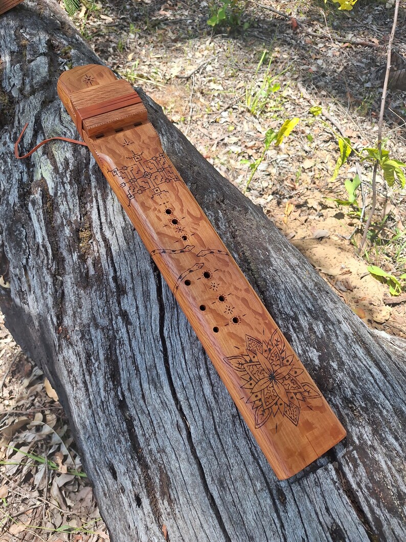 May include: A wooden flute with intricate carvings and a mandala design. The flute has a series of holes along its length and is resting on a tree trunk.
