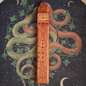 May include: A wooden flute with intricate carvings and a geometric design. The flute is made of light brown wood and has a dark brown stain. The flute is about 12 inches long and has a diameter of about 2 inches.