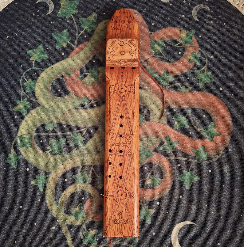 May include: A wooden flute with intricate carvings and a geometric design. The flute is made of light brown wood and has a dark brown stain. The flute is about 12 inches long and has a diameter of about 2 inches.