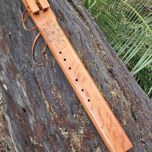 May include: A handcrafted wooden flute with a natural finish, featuring carved geometric designs and six finger holes. The instrument rests on a weathered log, showcasing its warm tones and intricate details.