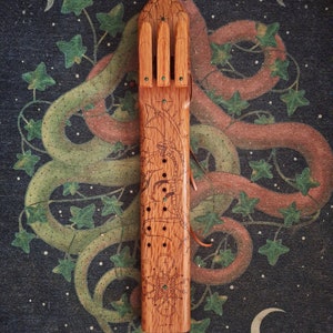May include: A wooden flute with a carved dragon design and green accents. The flute has a series of holes along the side and is decorated with a geometric pattern at the bottom.