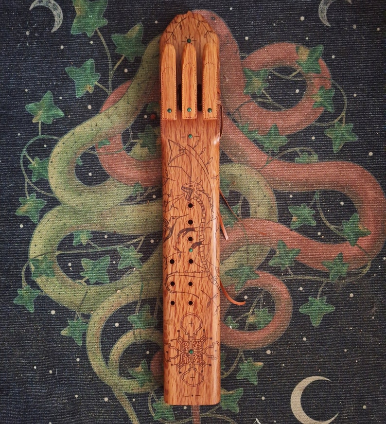 May include: A wooden flute with a carved dragon design and green accents. The flute has a series of holes along the side and is decorated with a geometric pattern at the bottom.