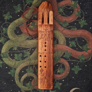 May include: A wooden flute with a carved design of a tree and leaves. The flute has a series of holes along the side and a decorative top.
