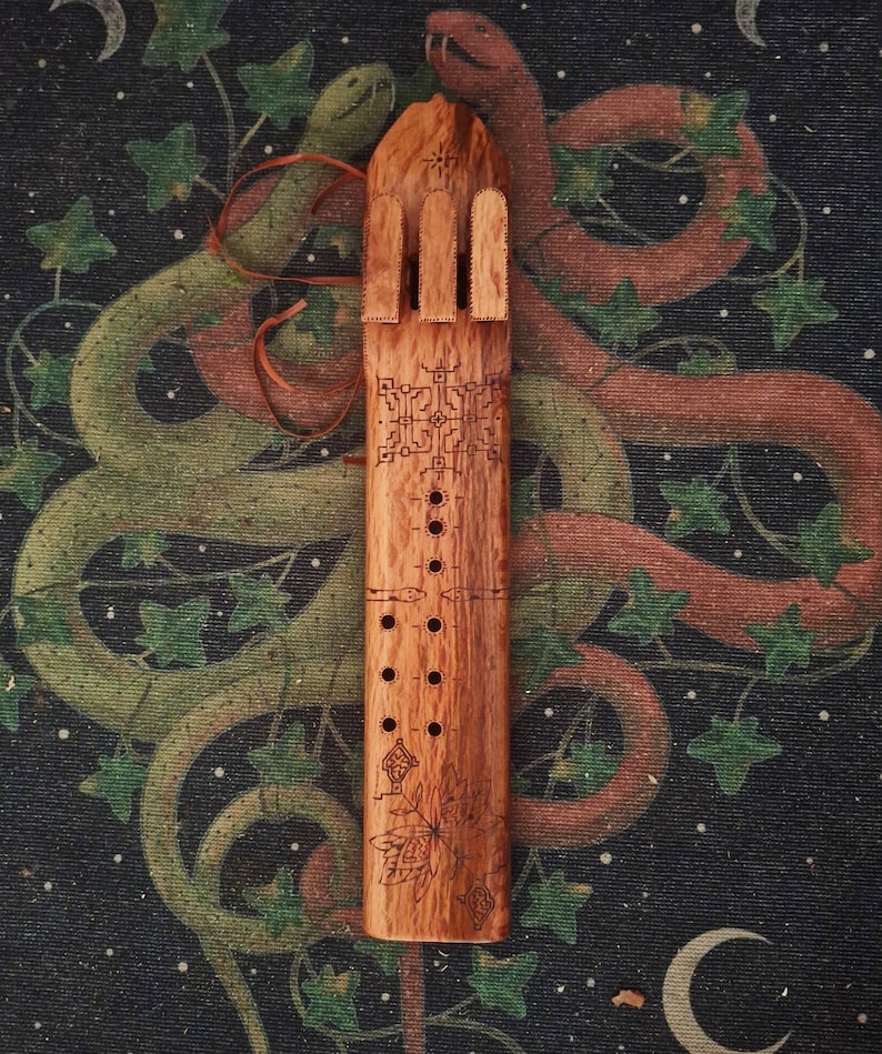 May include: A wooden flute with a carved design of a tree and leaves. The flute has a series of holes along the side and a decorative top.