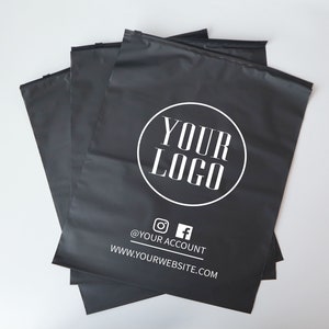 Op de afbeelding: Een stapel zwarte poly mailers met een wit cirkelvormig logo met de tekst "YOUR LOGO" en de tekst "@YOUR ACCOUNT" en "WWW.YOURWEBSITE.COM" onder het logo.