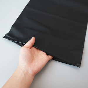 Op de afbeelding: Een zwarte plastic zak met een ritssluiting. De zak wordt opengehouden door een hand.