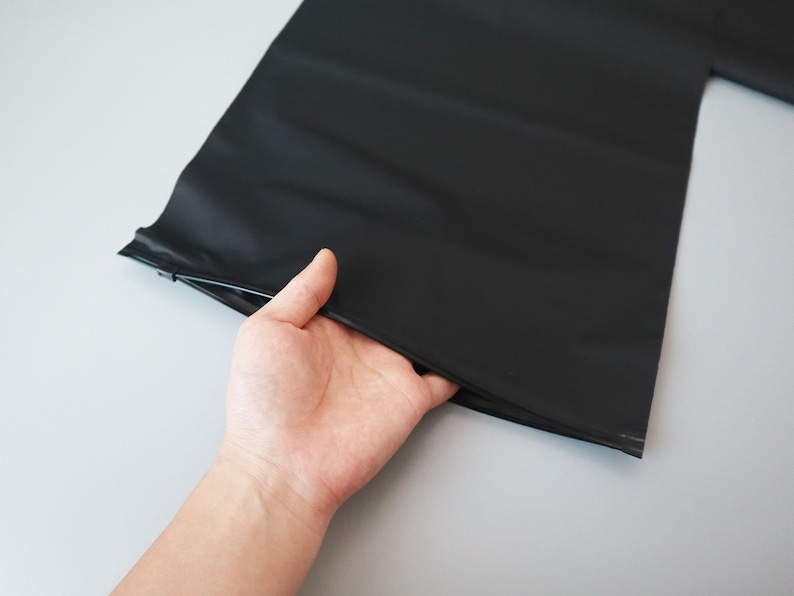 Op de afbeelding: Een zwarte plastic zak met een ritssluiting. De zak wordt opengehouden door een hand.