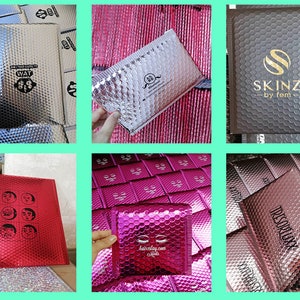 May include: Assortment of silver, red, and rose gold bubble mailers with various logos printed on them. The logos include "WAT", "SKINZ - by fem", "lashtastic.com", and "TRESORLUX".