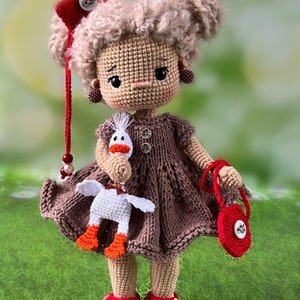 May include: A crocheted doll with brown hair, wearing a brown dress, red shoes, and a red bow. The doll is holding a white crocheted goose and a red purse.