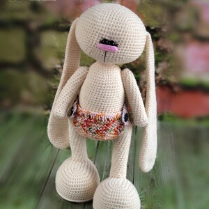 K&ouml;nnte beinhalten: Ein geh&auml;keltes Hasenspielzeug mit langen Ohren, einer rosa Nase und schwarzen Augen. Der Hase tr&auml;gt eine bunte Windel und steht auf einer Holzoberfl&auml;che. @soni_toys Irina Tarasova