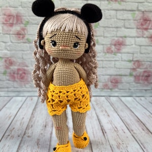 May include: A crocheted doll with blonde hair, wearing black mouse ears, a yellow crocheted skirt, and yellow crocheted shoes.