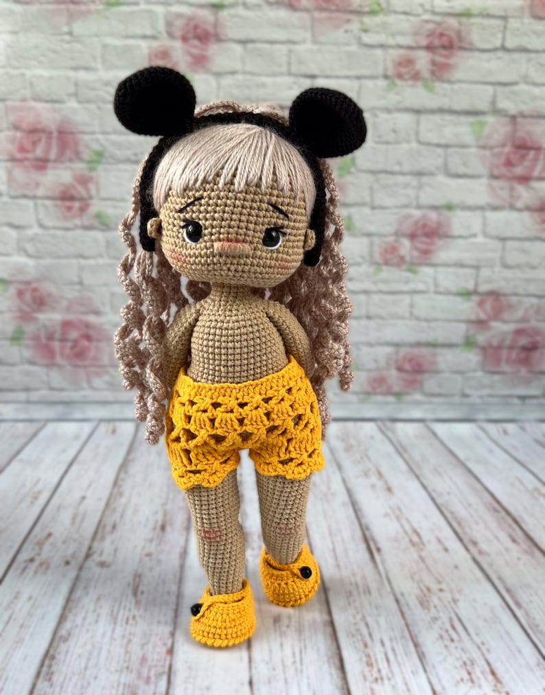 May include: A crocheted doll with blonde hair, wearing black mouse ears, a yellow crocheted skirt, and yellow crocheted shoes.