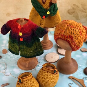 K&ouml;nnte beinhalten: Ein Set gestrickter Puppenkleidung in Herbstfarben, bestehend aus einem Kleid, einem Cardigan, einer M&uuml;tze und Stiefeletten. Die Kleidung wird auf Holzpuppen und Kleiderb&uuml;geln pr&auml;sentiert. @soni_toys Irina Tarasova