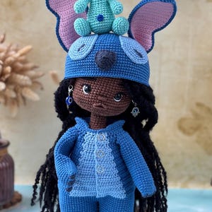 Pu&ograve; includere: Bambola all'uncinetto fatta a mano in blu, che assomiglia a un personaggio con grandi orecchie e una piccola creatura blu sulla testa. La bambola ha i capelli neri e indossa un completo blu. La bambola &egrave; alta circa 25 cm.