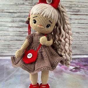 May include: A crocheted doll with blonde hair, a red bow, a brown dress, a red purse, and red shoes.