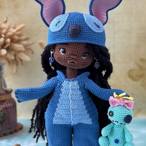 Pu&ograve; includere: Bambola all'uncinetto fatta a mano con un costume blu di Stitch, con grandi orecchie e un cappello abbinato. La bambola ha capelli neri, orecchini e tiene in mano una bambola Stitch pi&ugrave; piccola. L'outfit include una giacca abbottonata e pantaloni.