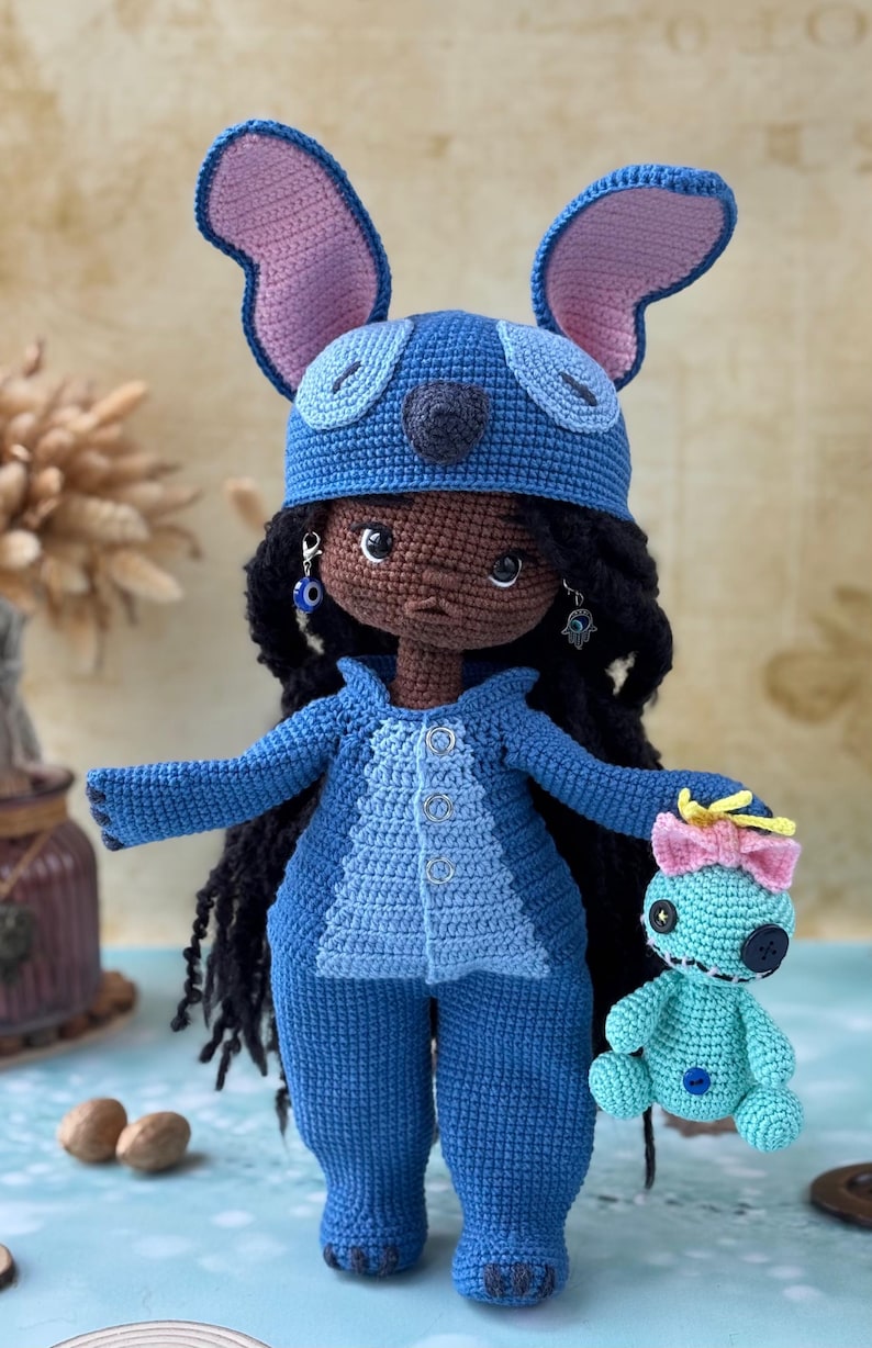 Pu&ograve; includere: Bambola all'uncinetto fatta a mano con un costume blu di Stitch, con grandi orecchie e un cappello abbinato. La bambola ha capelli neri, orecchini e tiene in mano una bambola Stitch pi&ugrave; piccola. L'outfit include una giacca abbottonata e pantaloni.