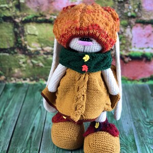 K&ouml;nnte beinhalten: Ein geh&auml;keltes H&auml;schen, das einen braunen und orangen Hut, einen gr&uuml;nen Schal und ein gelbes Kleid tr&auml;gt. Das H&auml;schen steht auf einer gr&uuml;nen Holzoberfl&auml;che. @soni_toys Ирина Тарасова