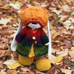 K&ouml;nnte beinhalten: Ein geh&auml;keltes H&auml;schen, das einen bunten Pullover, eine M&uuml;tze und Schuhe tr&auml;gt. Das H&auml;schen steht auf einem Bett aus Herbstlaub. Der Text '@soni_toys' und 'Юлия Тарасова' ist im Bild zu sehen.