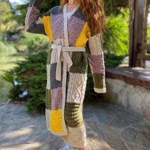 May include: A long, patchwork cardigan in various colours including yellow, green, and purple. The cardigan has a belt and is worn with white trainers. The knitted design features different textures and patterns.