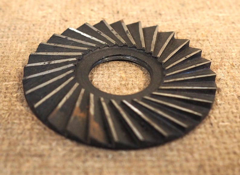 May include: A circular, dark metal gear with angled teeth and a central hole. The gear's teeth have a silver-colored edge, and the overall design suggests a mechanical or industrial component.
