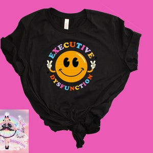 Può includere: Maglietta nera con una faccia sorridente gialla e il testo "Disfunzione Esecutiva" in colori arcobaleno attorno al viso.
