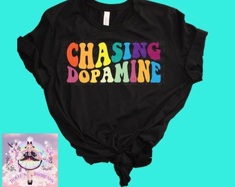 May include: Black t-shirt with the text "CHASING DOPAMINE" in rainbow colors. The text is in a retro font style.
