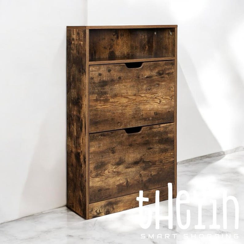 K&ouml;nnte beinhalten: Ein brauner Schuhschrank aus Holz mit zwei Schubladen und einem Regal. Der Schuhschrank hat eine Antik-Holz-Optik und steht auf einem wei&szlig;en Fliesenboden.