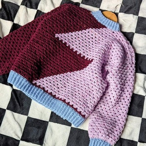 May include: A crocheted sweater with a geometric design in shades of burgundy, lavender, and light blue.